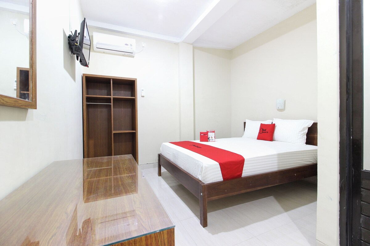 A bedroom with a wooden bed, a red and white bedspread, a wooden wardrobe, a mirror, and an air conditioning unit.