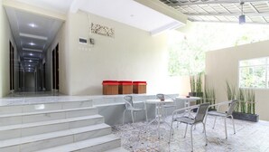 Un moderno vestíbulo de hotel con piso de baldosas, una escalera que conduce a los pisos superiores, una zona de estar con sillas y una mesa, y un amplio ventanal que proporciona luz natural.