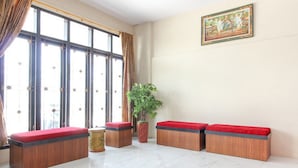 Amplia habitación con ventanas grandes, una planta en maceta y dos bancos de madera con cojines rojos.