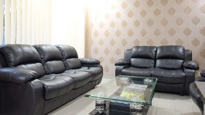 Ein Wohnzimmer mit zwei schwarzen Ledersofas, einem Glastisch und einer Wand mit Musterung.