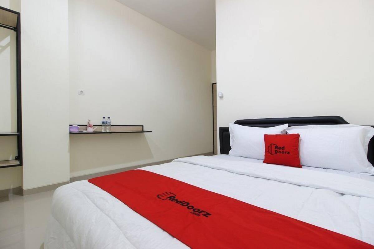 Een hotelkamer met een bed, een rode deken, een kussen met het logo 'Red Doorz' en een plank met toiletartikelen.