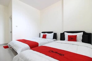 Ett hotellrum med två sängar, där varje säng har vita sängkläder och röda detaljer, samt en röd logotyp på sängarna.