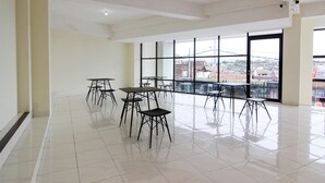 A spacious indoor area with multiple tables and chairs, large windows offering a view of the city, and a tiled floor. - RedDoorz near Malioboro Mall 2 (Yogyakarta)