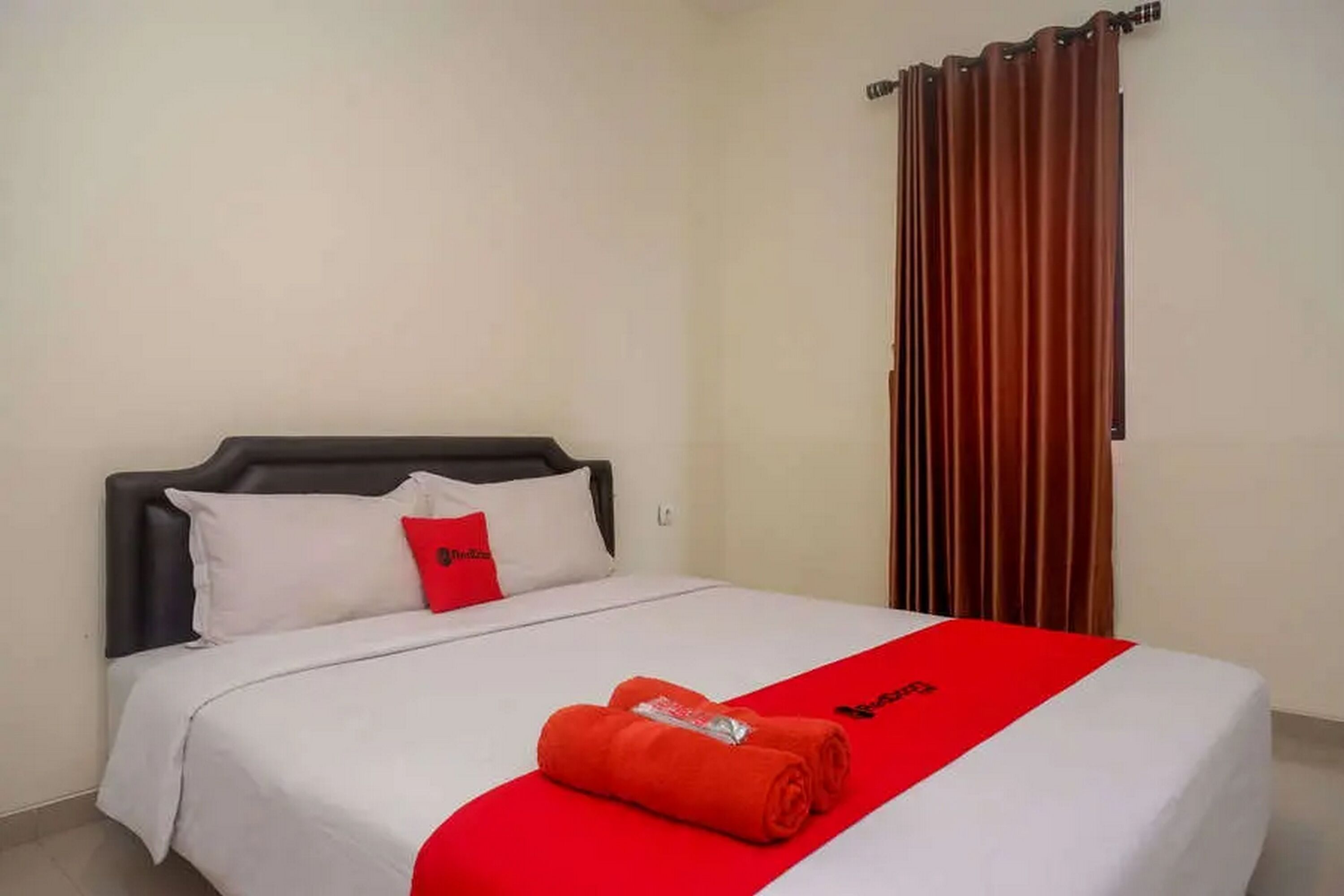 Une chambre d’hôtel avec un lit, du linge de lit blanc, une serviette rouge et un rideau.