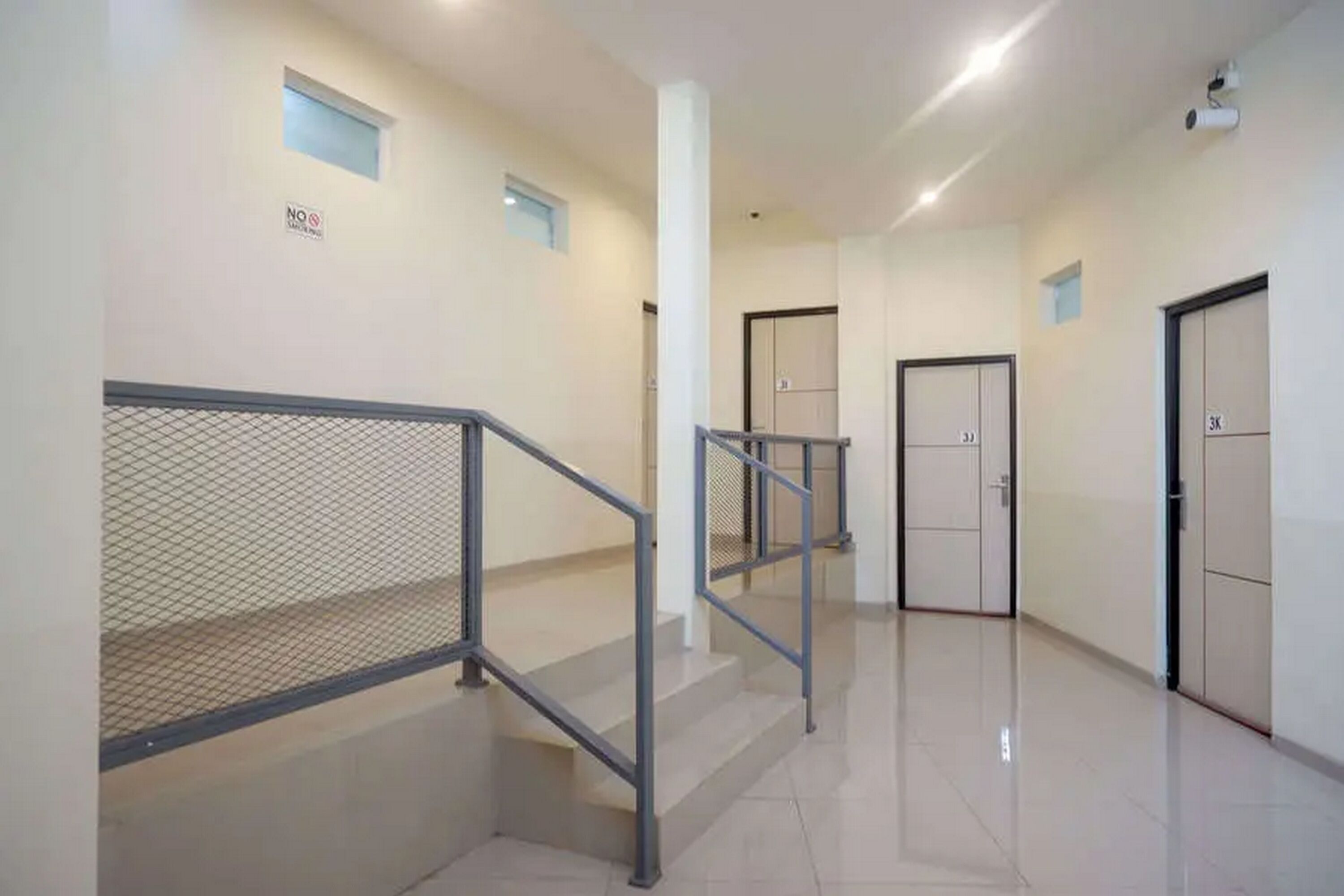 A clean, modern hallway with a metal staircase, doors, and a "NO Smoking" sign.