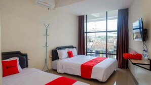 A hotel room with two beds, a TV, and a window with a city view. - RedDoorz near Malioboro Mall 2 (Yogyakarta)
