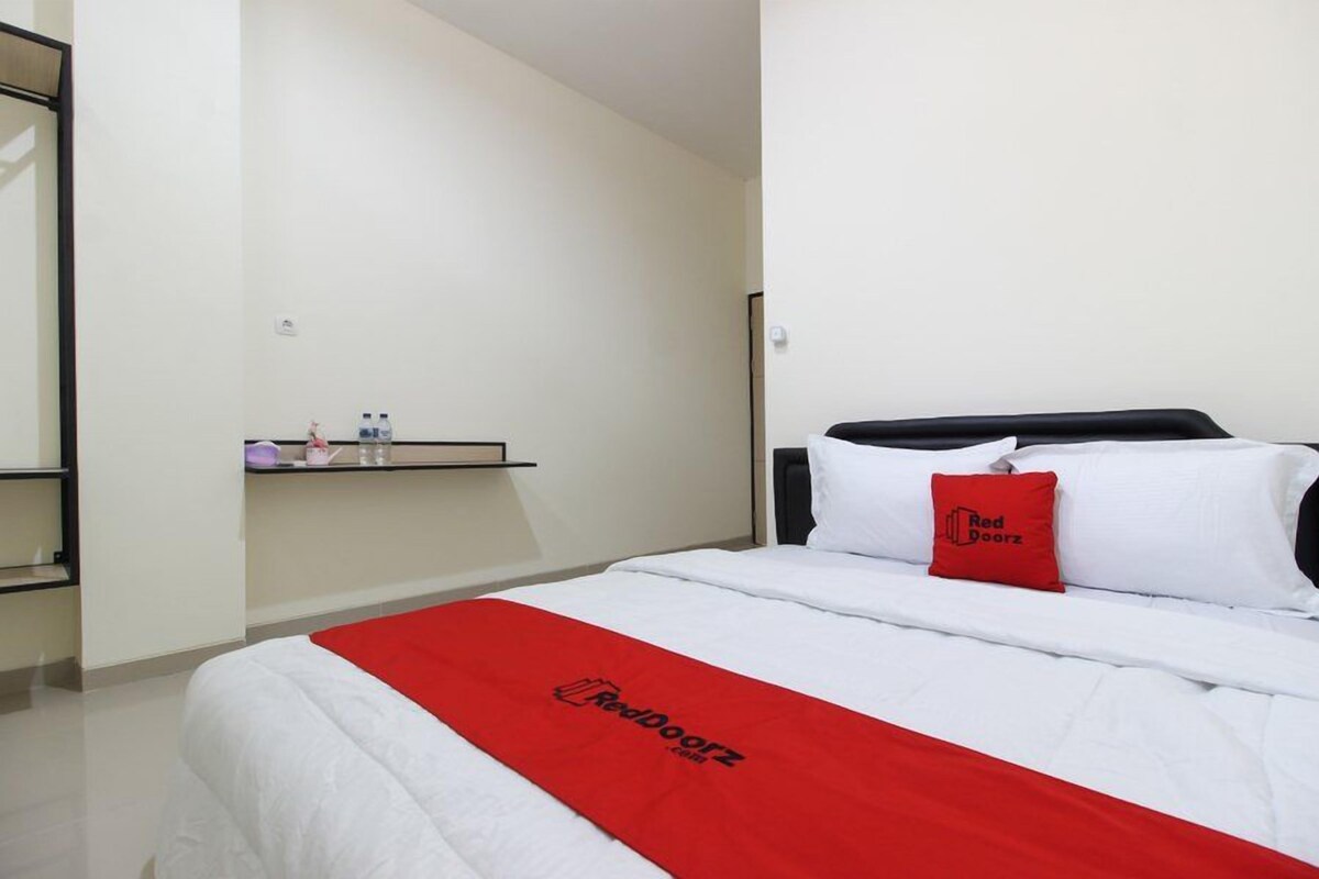 Een hotelkamer met een bed, een rode deken, een kussen met het logo 'Red Doorz' en een plank met toiletartikelen.
