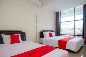 Ett hotellrum med två sängar, båda med vita sängkläder och röda detaljer, ett stort fönster med utsikt och en klädställning.
