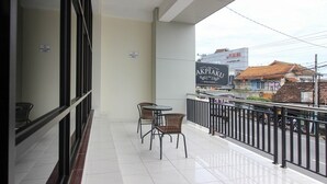 A balcony with two wicker chairs and a small table, overlooking a street with buildings and a sign for 'AKPIAK'. - RedDoorz near Malioboro Mall 2 (Yogyakarta)