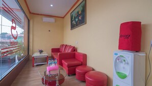 A hotel room with a red sofa set, a glass coffee table, a small side table with water bottles, and a water dispenser. - RedDoorz @ Batu Aji Batam 2 (Batam)