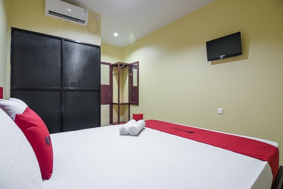 A hotel room with a bed, a TV, an air conditioning unit, and a wardrobe.