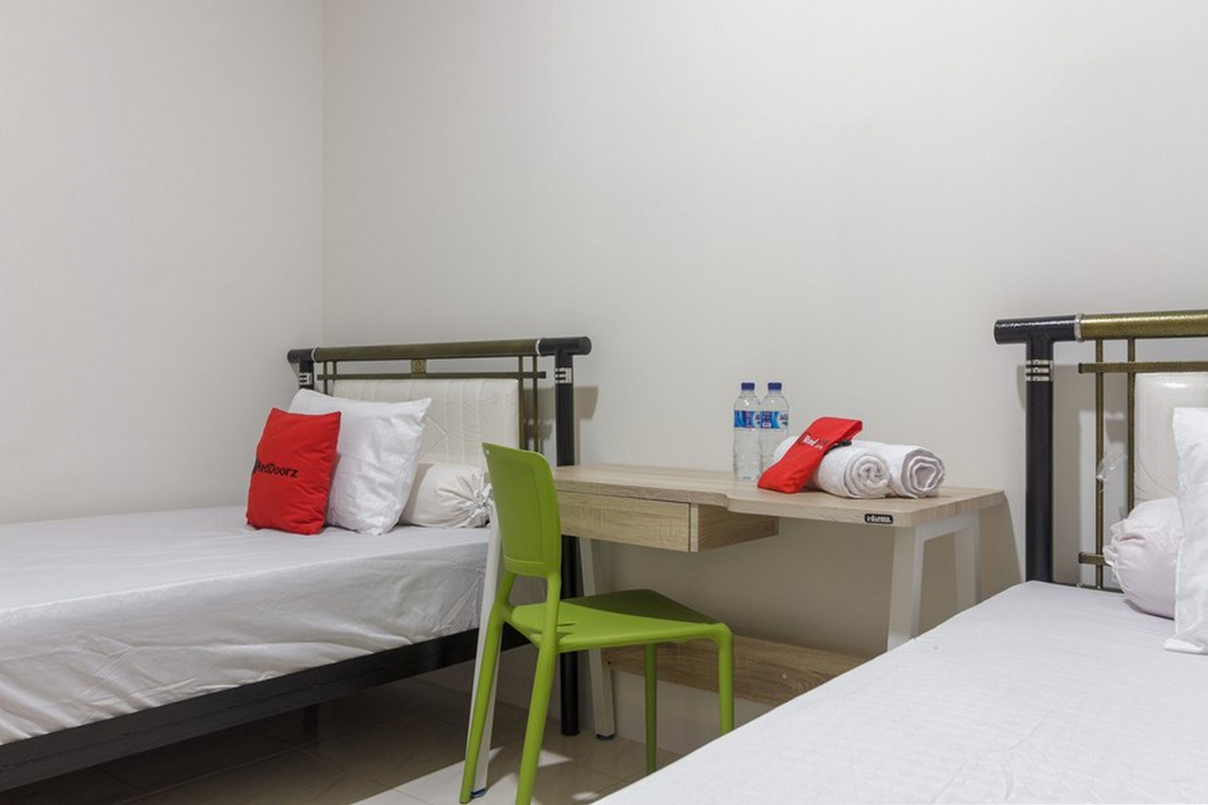 Une chambre d’hôtel avec deux lits simples, un bureau, une chaise verte et une petite table avec des serviettes et des articles de toilette.
