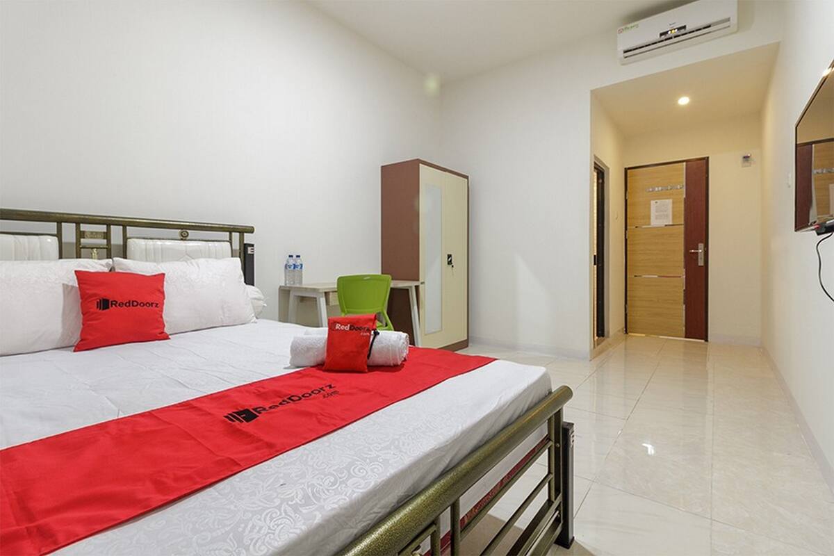 A hotel room with a bed, a desk, a chair, a wardrobe, and a door.