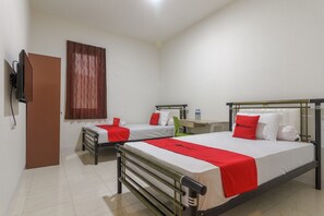 Una camera d'albergo con due letti singoli, una scrivania e un televisore.