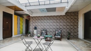 Un vaste espace intérieur doté d’un haut plafond, d’un mur en briques et d’une verrière. On y trouve des chaises pliantes et une petite table sur laquelle est posée une plante.