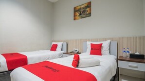 Une chambre d’hôtel avec deux lits, chacun recouvert d’une couverture rouge et blanche, une table de chevet avec un téléphone et des bouteilles d’eau, et un tableau accroché au mur.