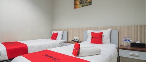 A hotel room with two beds, each with a red and white bedspread, a nightstand with a phone and water bottles, and a painting on the wall.