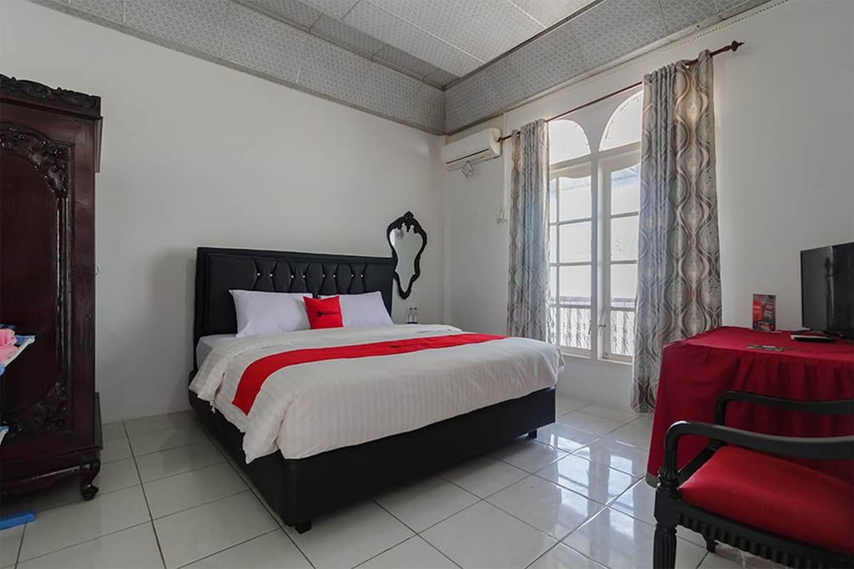 A bedroom with a large bed, a wooden wardrobe, a television, and a red table.