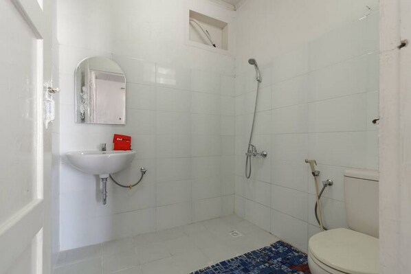 A small, clean bathroom with white tiles, a sink, a toilet, and a shower. - RedDoorz Syariah near Universitas Negeri Padang (Padang)