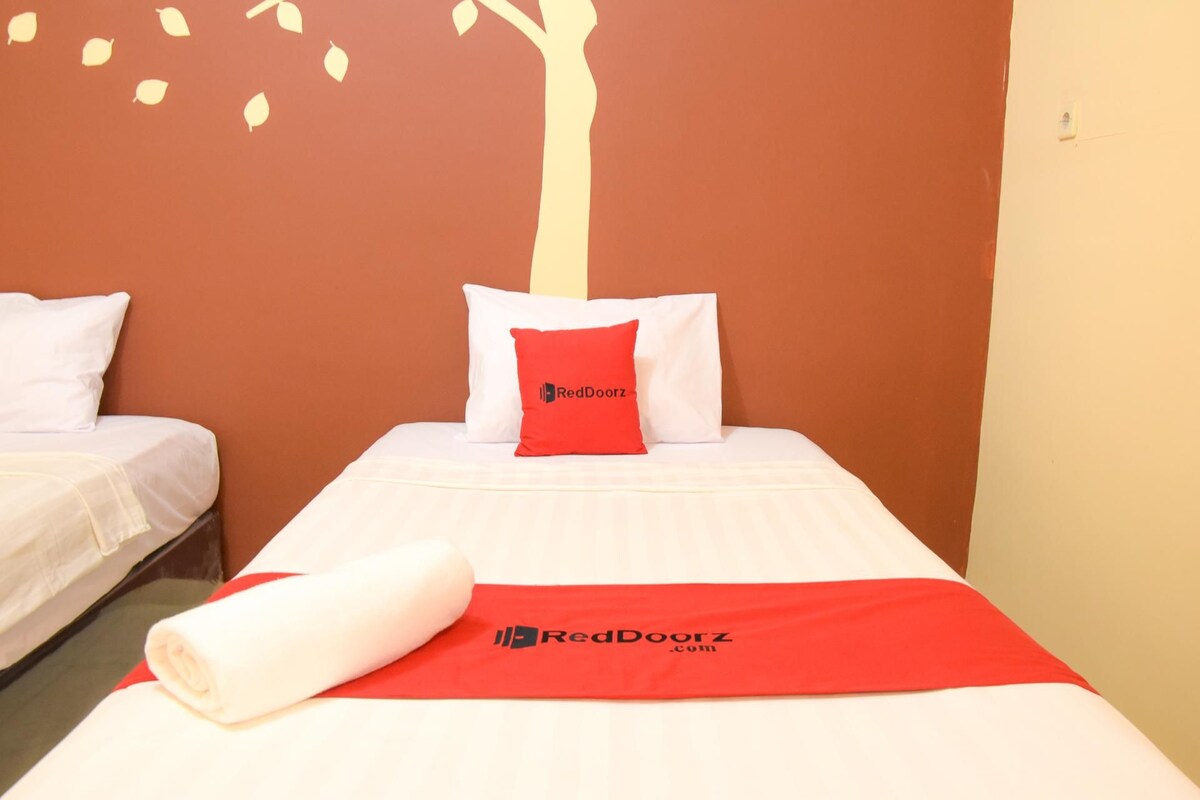 Una habitación de hotel con una cama, un almohadón rojo con el logotipo de RedDoorz y una toalla roja.