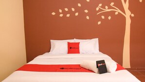 A neatly made bed with white bedding and a red blanket, a red pillow, and a black item on the bed. - RedDoorz near Terminal A Adisucipto Airport (Kalasan)