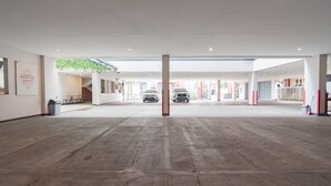 A spacious indoor area with a concrete floor, a central pillar, and a view of parked cars through a glass wall. - RedDoorz Plus @ Dago Pojok 3 (Bandung)