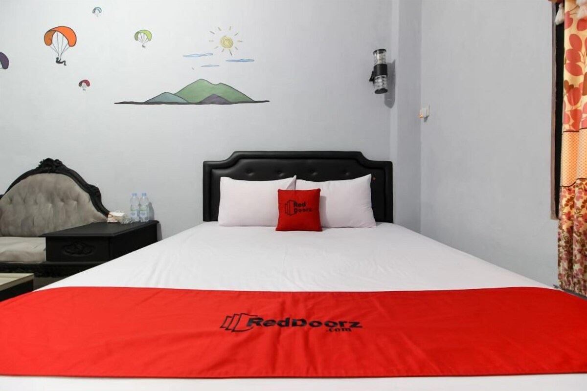 Quarto de hotel com cama, mesa de cabeceira, abajur e parede com mural.