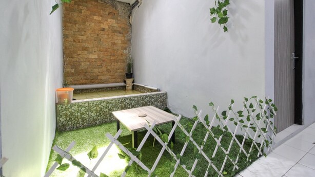 A small, enclosed outdoor space with a brick wall, a white door, and a small table. - RedDoorz near Graha Saba UGM (Depok)