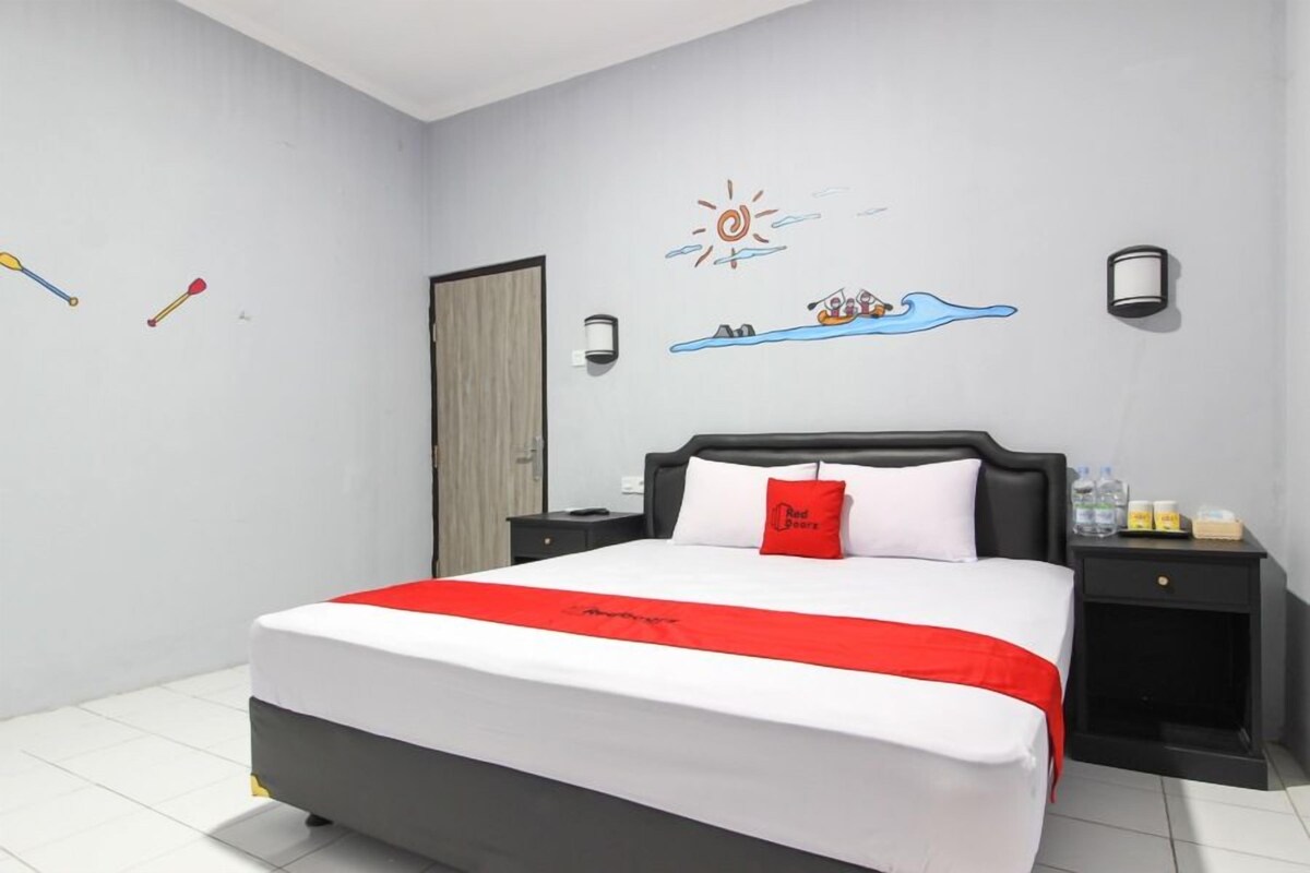 A hotel room with a large bed, a nightstand, a wall with a sun and wave decoration, and a door.