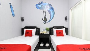 A hotel room with two beds, each with a red blanket and pillow, a small table with a plant, and a wall mural of a diver. - RedDoorz near Graha Saba UGM (Depok)