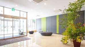A modern lobby with a glass entrance, seating areas, and a large potted plant.