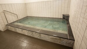 A rectangular hot tub with a glass edge, surrounded by tiled walls and a tiled floor.