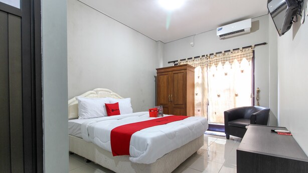 Una habitación de hotel con cama, escritorio, silla, armario y ventana con cortinas.