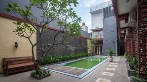 Un patio con piscina, un banco de madera y un árbol en maceta.