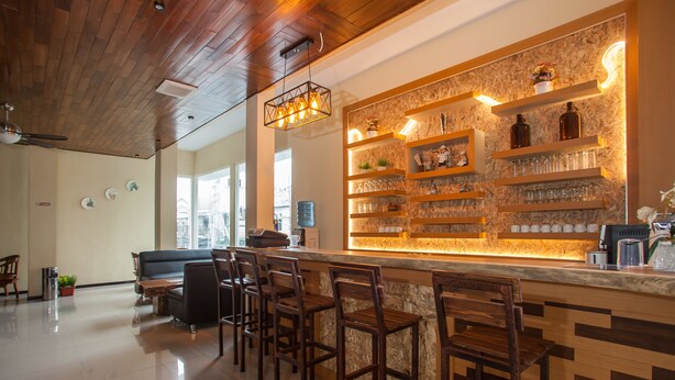Una zona de bar con sillas de madera y estanterías llenas de vasos y botellas.