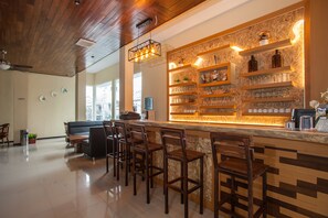 Una zona de bar con sillas de madera y estanterías llenas de vasos y botellas.