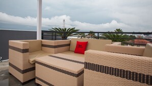 A covered outdoor seating area with wicker furniture and a red pillow, overlooking a cityscape. - RedDoorz Plus near Politeknik Negeri Malang (Malang)