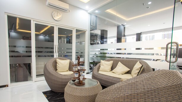 A modern living area with wicker furniture, a glass coffee table, and a view of parked cars outside. - RedDoorz Plus near Politeknik Negeri Malang (Malang)