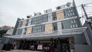 A modern building with a covered parking area, multiple floors, and a mix of stone and metal exterior. - RedDoorz Plus near Politeknik Negeri Malang (Malang)
