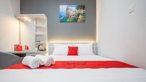 A neatly made bed with a red blanket and pillows, a white wall with a framed picture, and a white shelf unit. - RedDoorz Plus near Politeknik Negeri Malang (Malang)