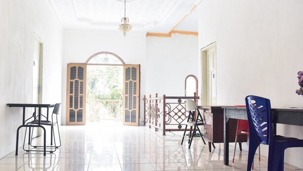 Um quarto espaçoso com piso de azulejos, uma escrivaninha de madeira, um computador, uma cadeira e uma porta decorativa com vista para o exterior.