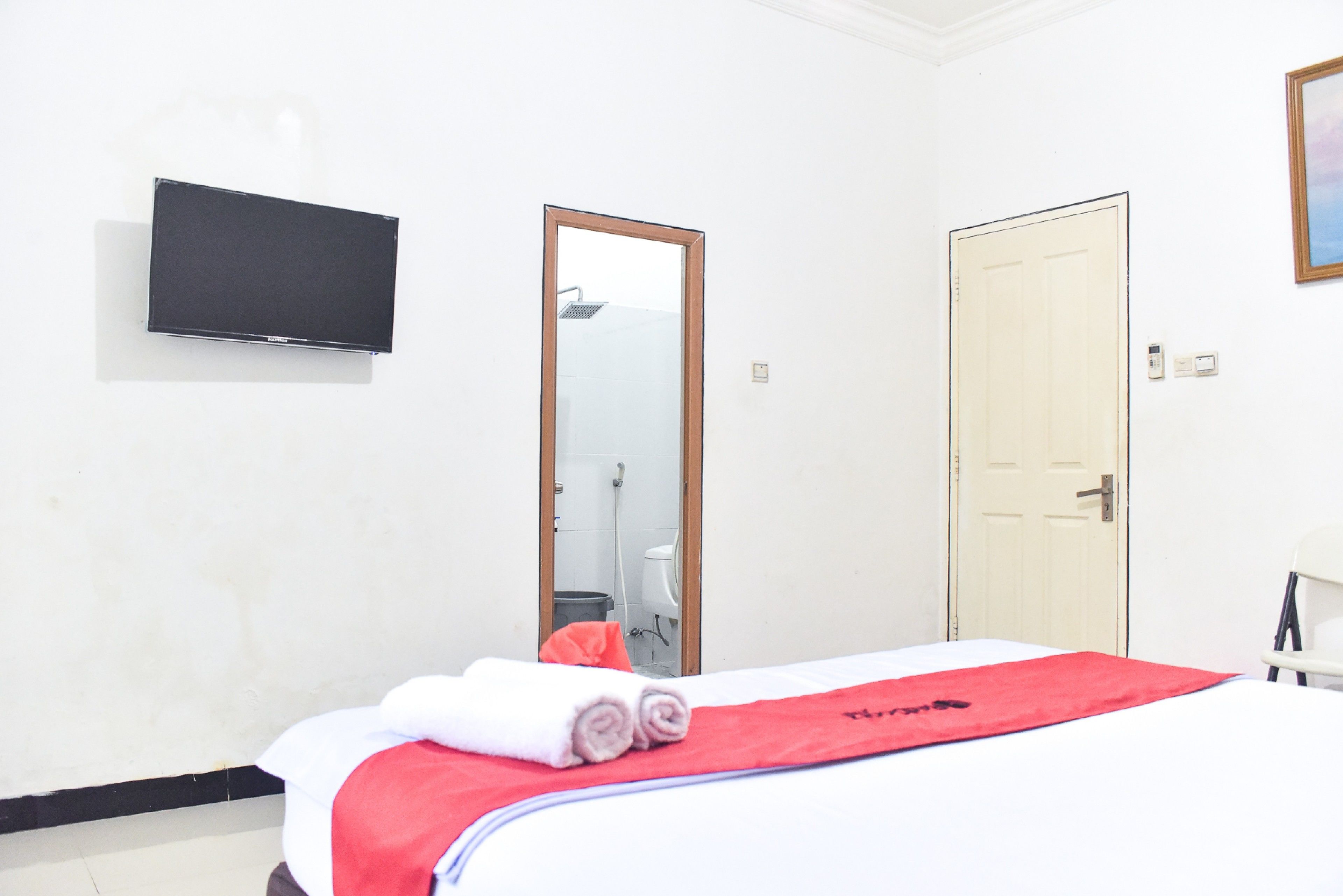 Una habitación de hotel con una cama, un televisor montado en la pared, un espejo y una puerta.
