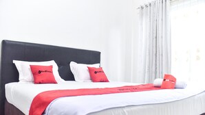 Cama bem arrumada com roupa de cama branca e vermelha, manta vermelha e duas almofadas com logotipo.