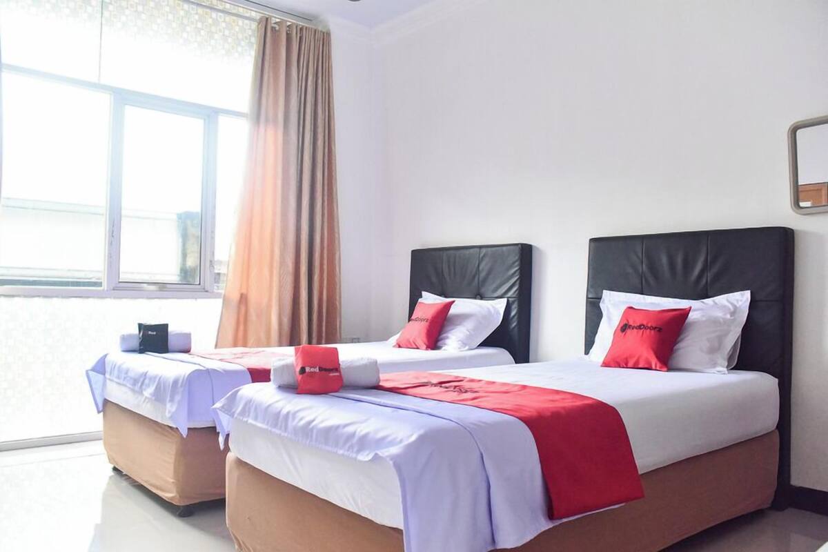 Hotellihuone, jossa on kaksi sänkyä. Jokaisessa sängyssä on pääty, valkoiset vuodevaatteet ja punaiset yksityiskohdat.