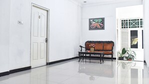 Um corredor com uma porta branca, um banco, um quadro emoldurado e uma janela com persianas.