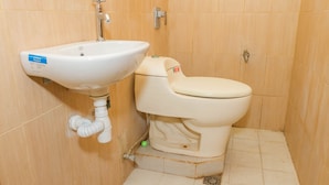 Un baño pequeño con lavamanos y retrete blancos, paredes de madera y piso de baldosas.