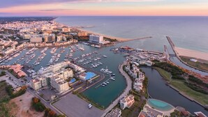 An aerial view of a coastal marina with numerous boats docked, surrounded by residential buildings and a bridge connecting to the mainland.
