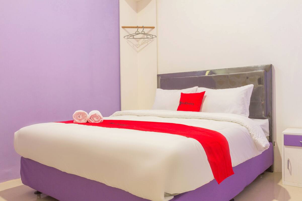 A neatly made bed with white and red bedding, a red pillow, and two rolled towels.