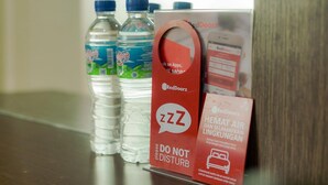 Un espace d’accueil d’hôtel avec des bouteilles d’eau, un panneau RedDoorz et un panneau « Ne pas déranger ».