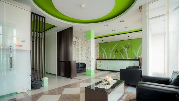 Un espace d’accueil moderne avec un sol à carreaux, un comptoir d’accueil, des canapés noirs et un mur d’accent vert.